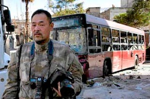 Japanese trucker Toshifumi Fujimoto holds his cameras in front of damaged buses in Aleppo's old city in Syria.