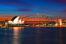 Two of Sydney's famous icons, the Sydney Opera House and Sydney Harbour Bridge lit up at dusk after a vivid sunset.