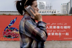 A Uygur woman walks past a propaganda sign in Urumqi, which reads: 'All different peoples should unite together just ...