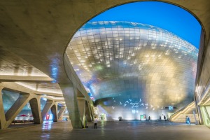 Dongdaemun Design Plaza - a Zaha Hadid-designed curving building of gleaming metal, lights up at night.